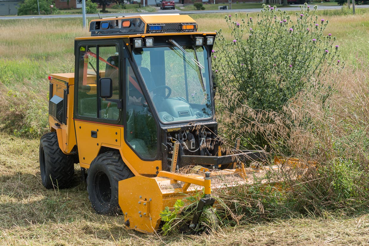 trackless vehicles front flail mower attachment on sidewalk municipal tractor mowing grass side front view