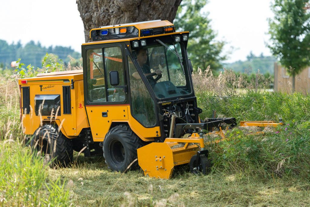 trackless vehicles front flail mower attachment on sidewalk municipal tractor mowing grass side view