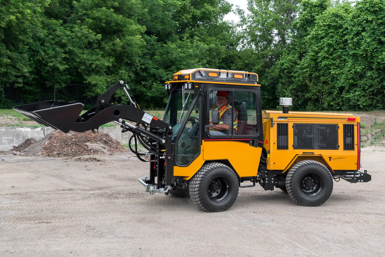 trackless vehicles front end loader attachment on sidewalk municipal tractor side view