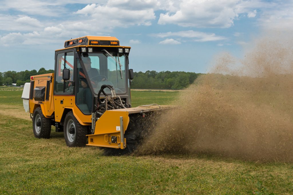 trackless vehicles power angle sweeper attachment on sidewalk municipal tractor moving dirt in field