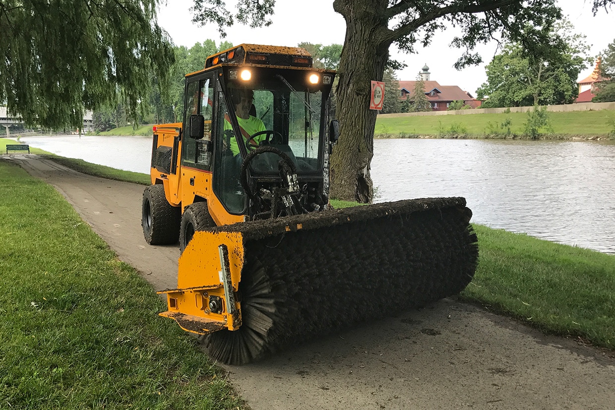 trackless vehicles power angle sweeper attachment on sidewalk municipal tractor muddy working in park front view